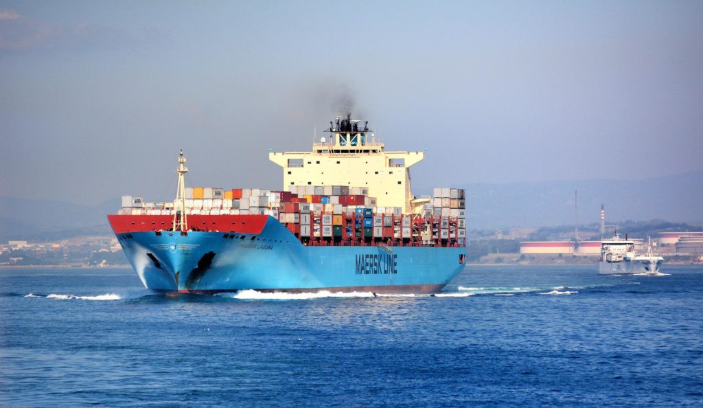 Na zdjęciu znajduje się statek kontenerowiec załadowany kolorowymi kontenerami, płynący po morzu.