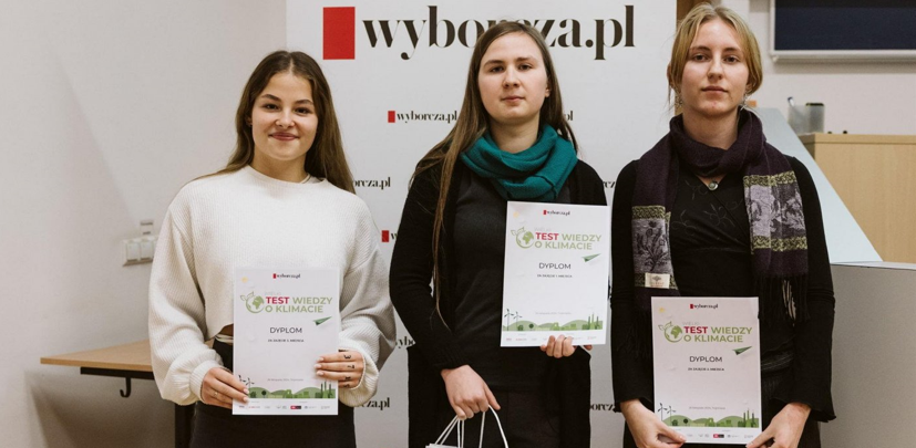 NAa zdjęciu znajdują się uczennice gdyńskiej "Trójjki" z nagrodami. Pierwsza od lewej ubrana jest w białą bluzkę, a dwie pozostałe - w czarne bluzki. Trzymają w dłoniach dyplomy i wyróżnienia. Stoją na tle bannera Wyborcza.pl